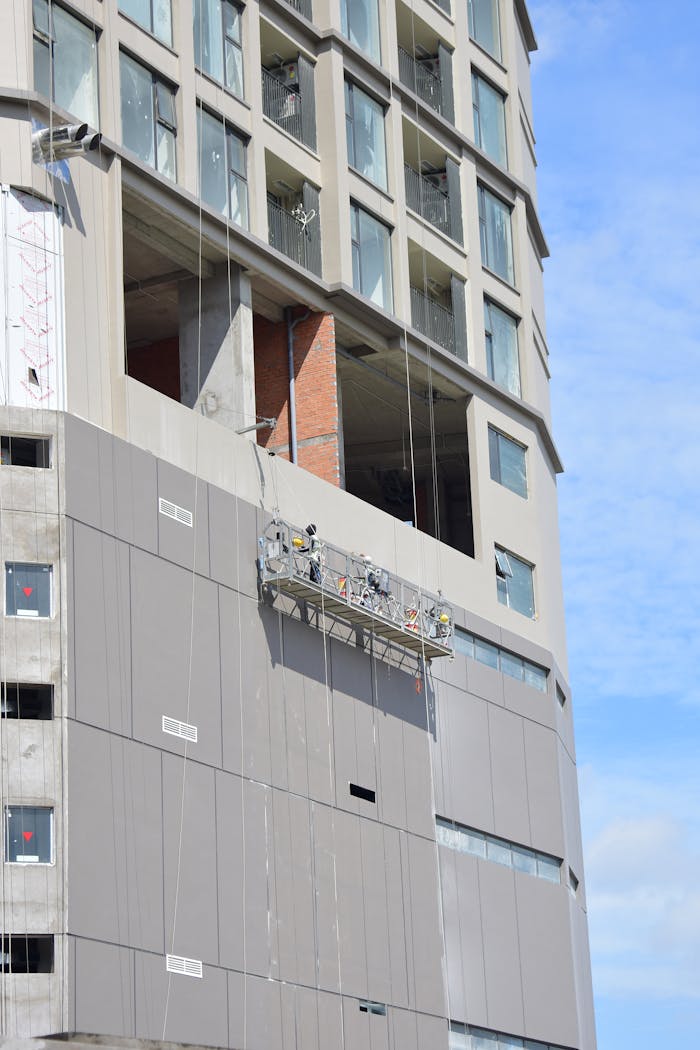 Construction workers on a suspended scaffold work on the facade of a high-rise building.